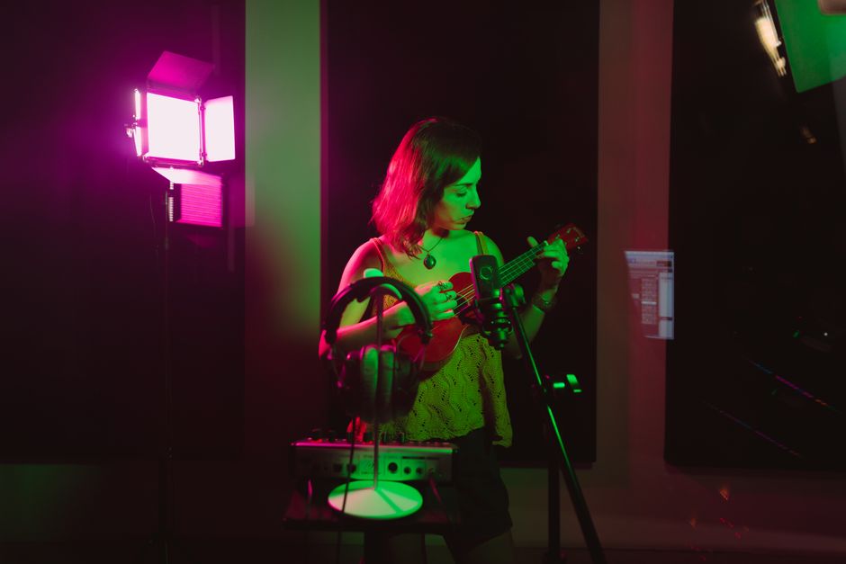Woman playing ukulele in a colorful recording studio setup.